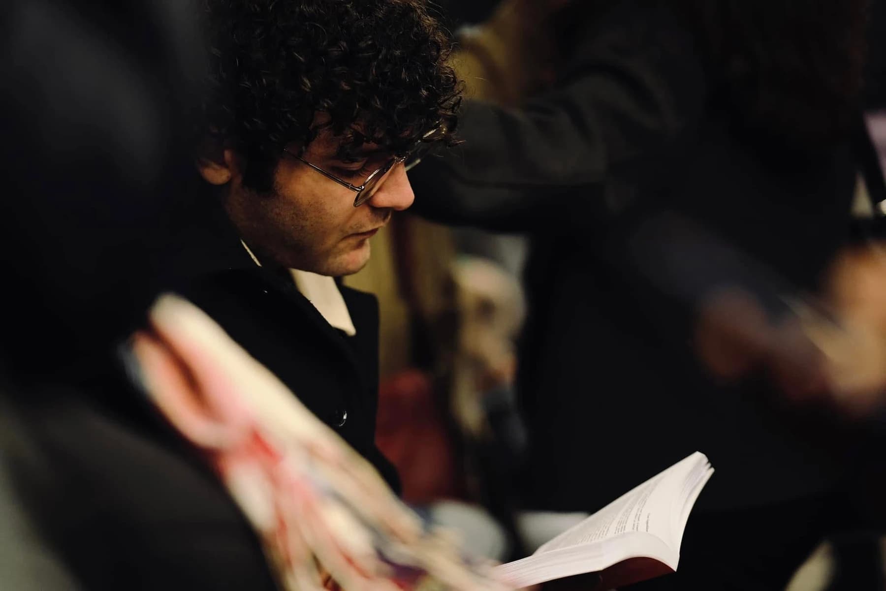 A candid portrait of a person reading, framed by soft foreground blur.