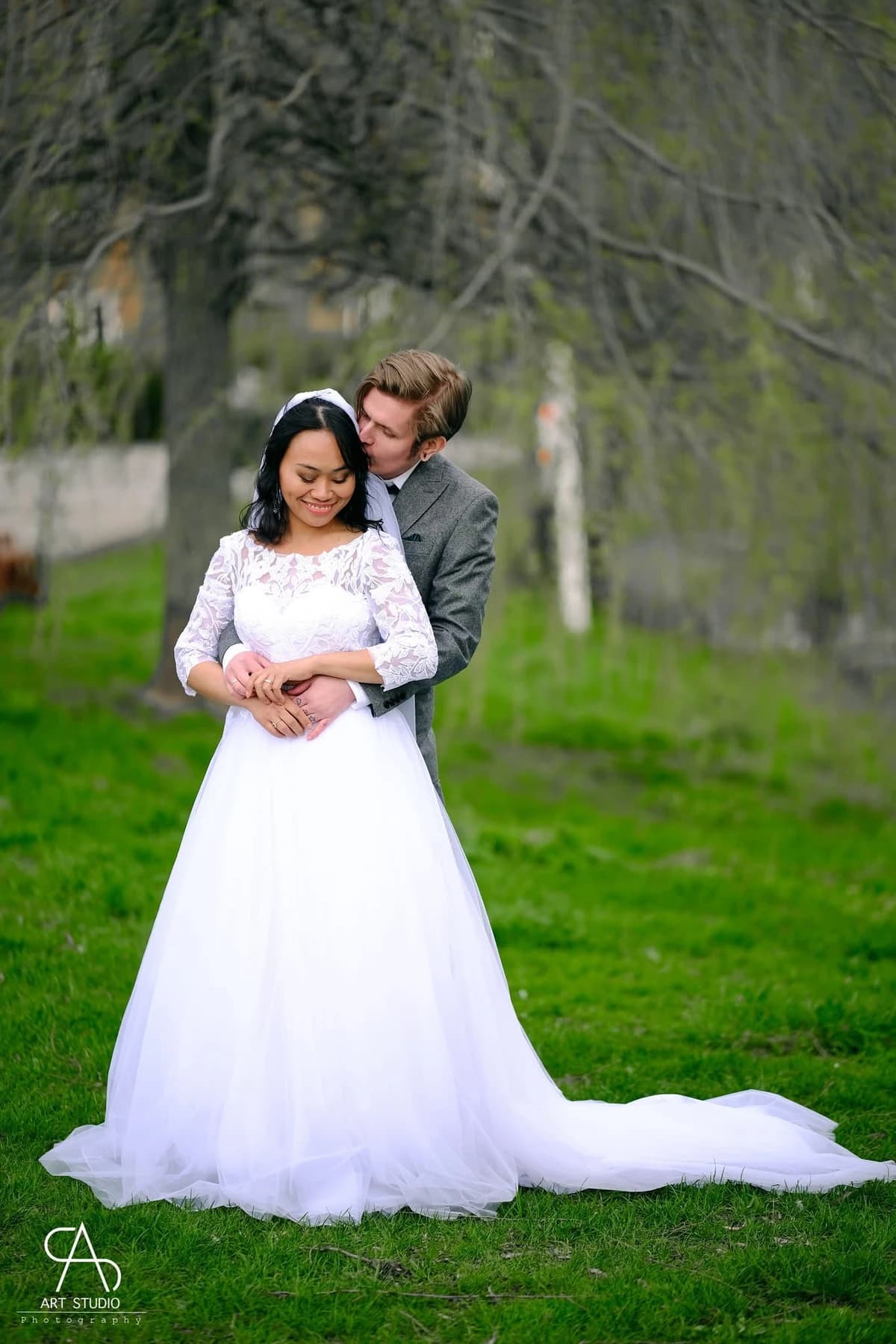A wedding couple embracing in a green garden, with the full bridal dress visible.