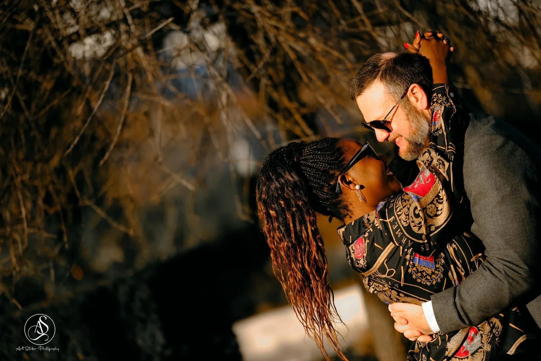 A couple embracing in warm golden light beneath trees.