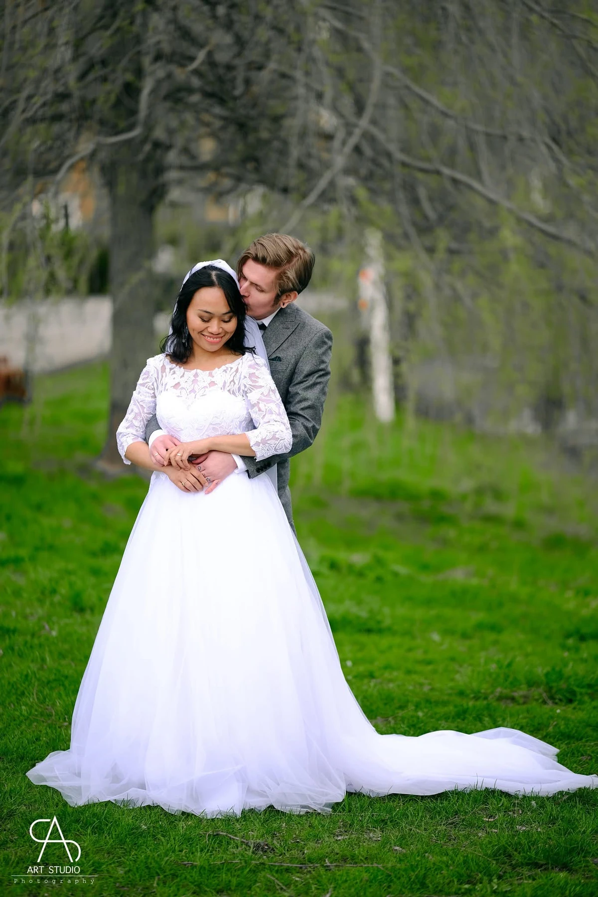 A wedding couple embracing in a green garden, with the full bridal dress visible.